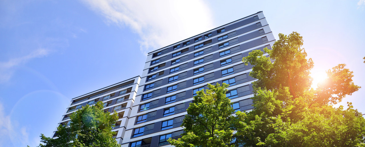 Edificio de apartamentos a contraluz, con el sol entre los árboles
